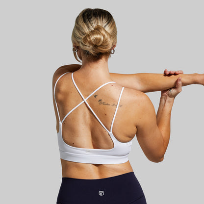Woman wearing a white sports bra and navy leggings on a gray background