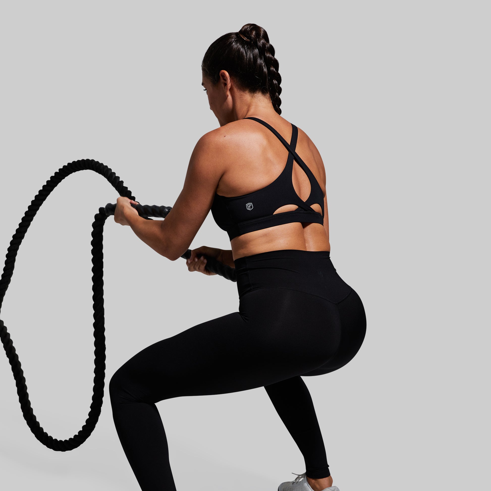 Person in black athletic wear holding a rope against a gray background