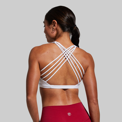 Woman wearing a white strappy sports bra and red leggings on a gray background