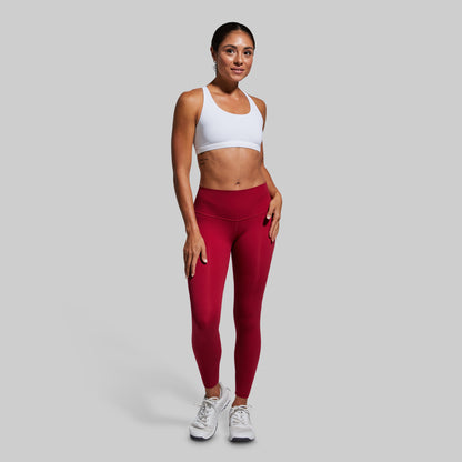 Woman wearing red leggings and a white sports bra on a gray background