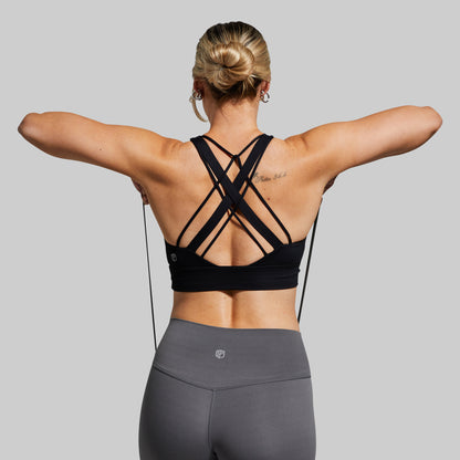 Person wearing a black sports bra and gray leggings on a plain background