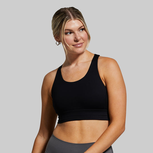 Woman wearing a black sports bra and gray leggings against a plain background