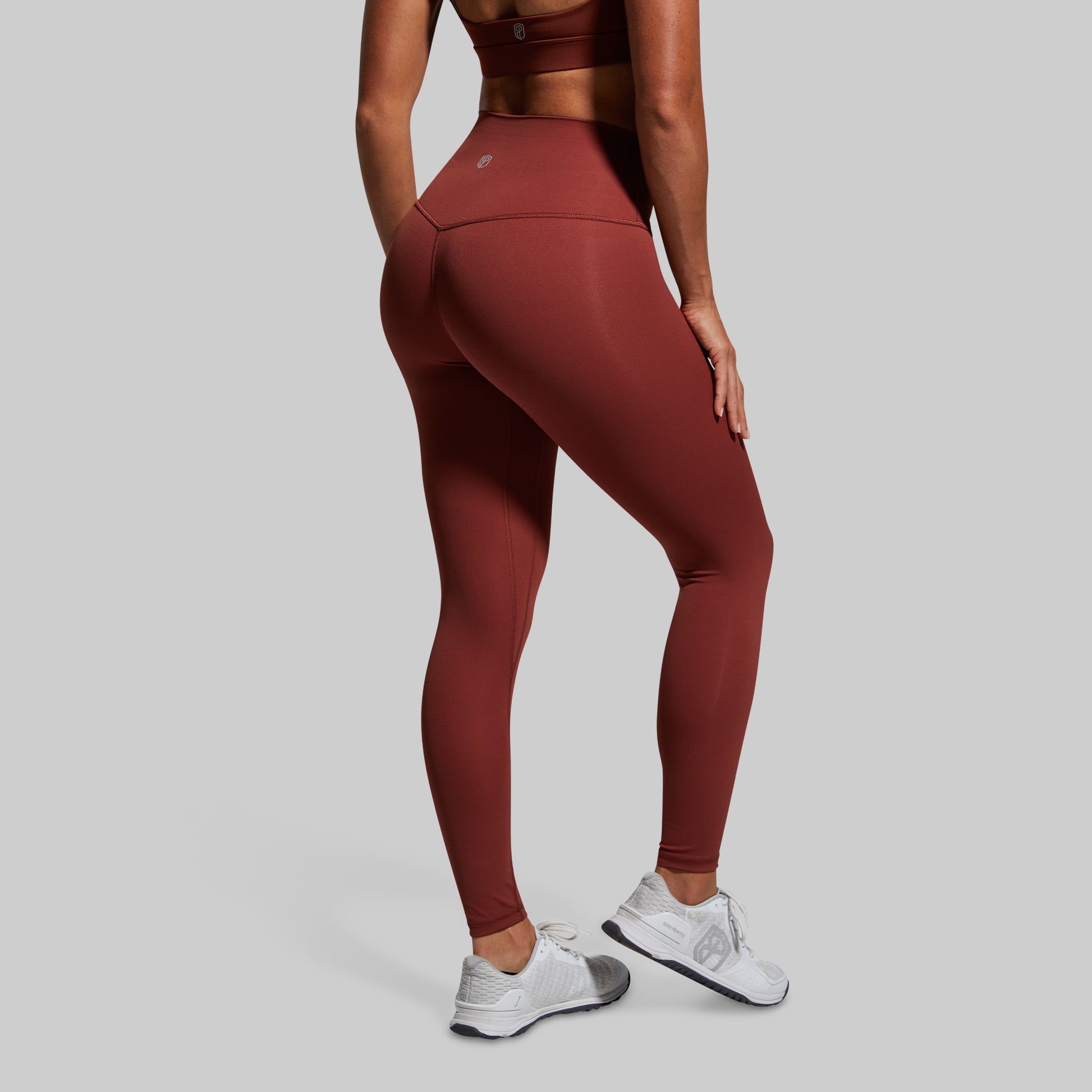 Person wearing maroon leggings and white sneakers on a gray background