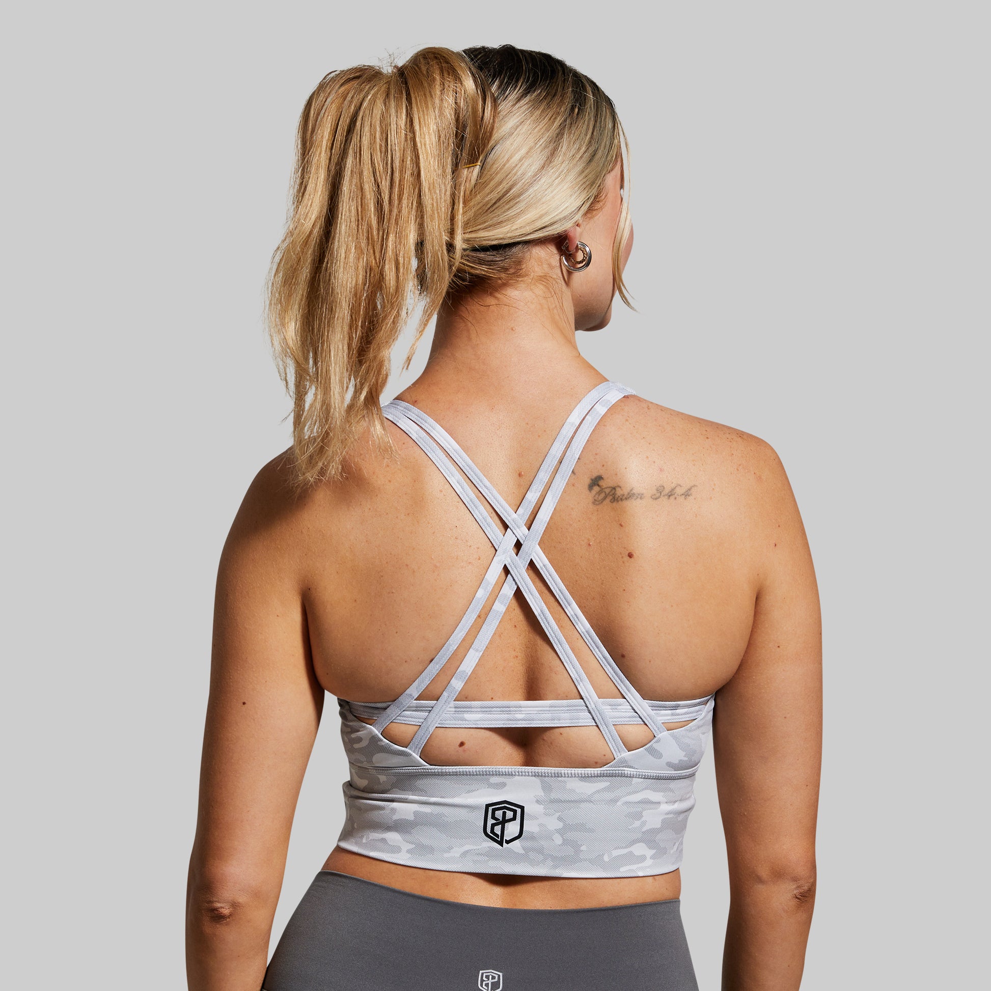 Woman wearing a gray sports bra with criss-cross straps on a plain background
