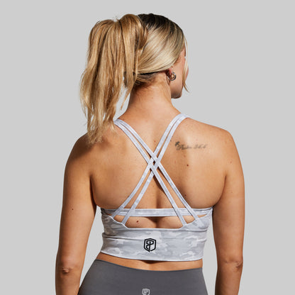 Woman wearing a gray sports bra with criss-cross straps on a plain background