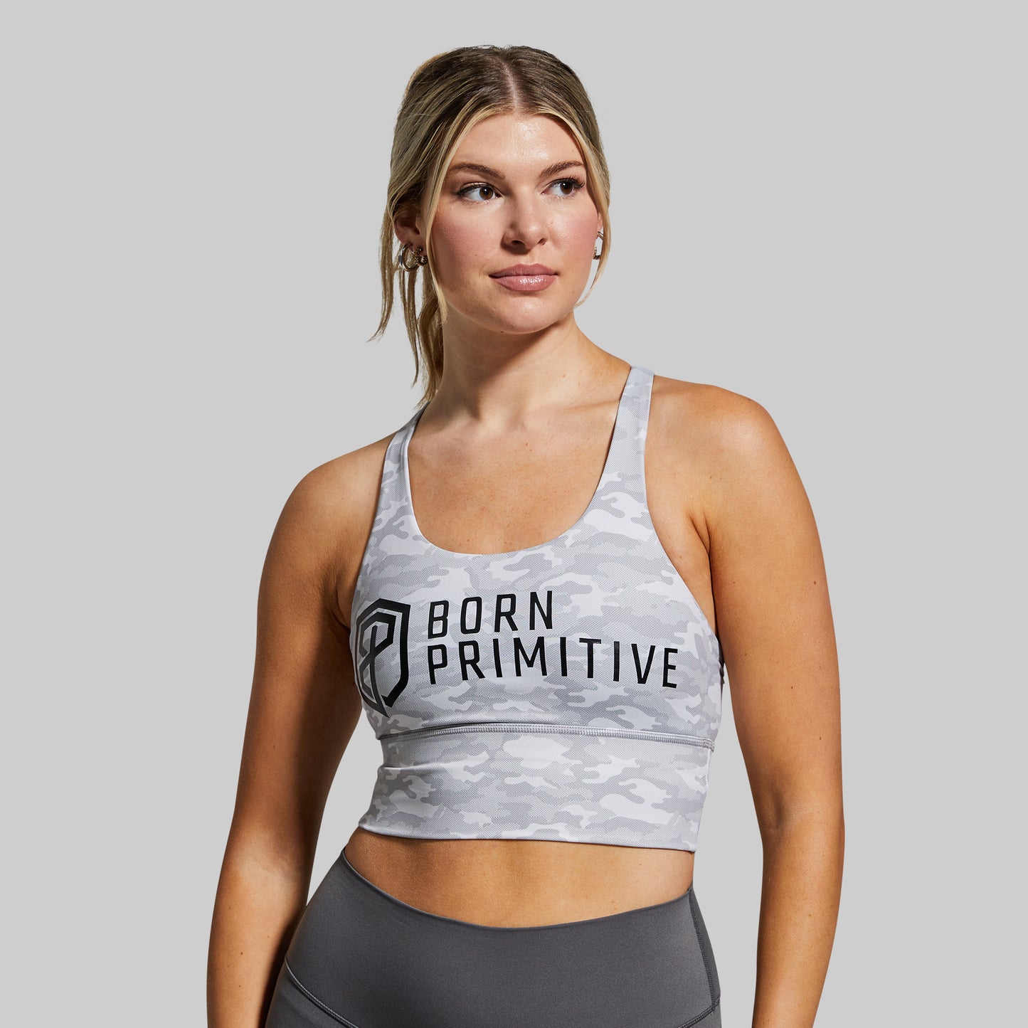 Woman wearing a sports bra with 'Born Primitive' branding on a gray background