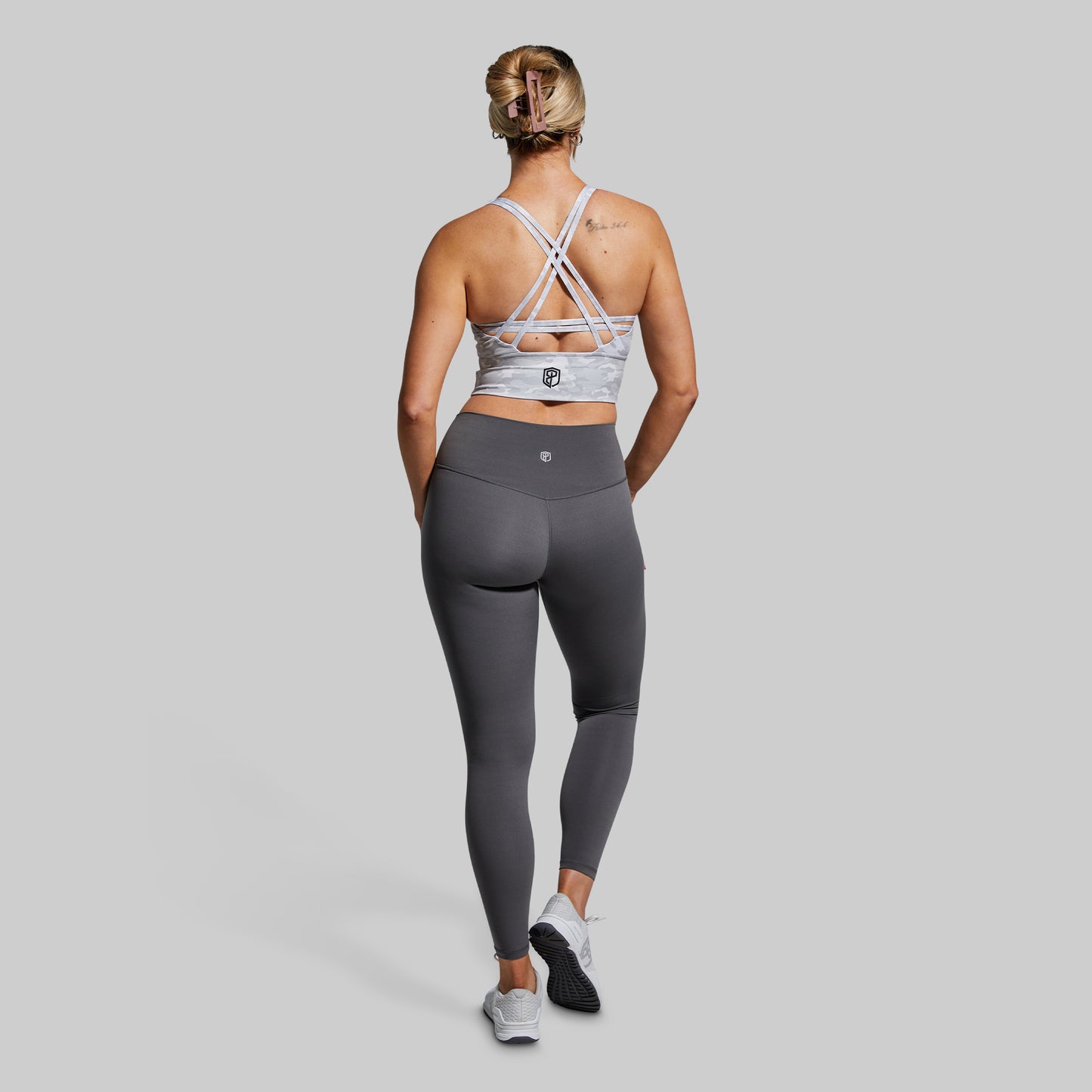 Woman wearing a sports bra and leggings on a plain background