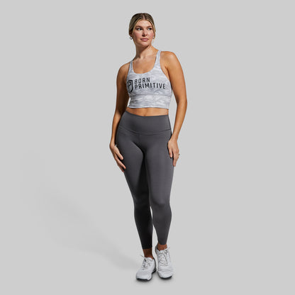 Woman wearing a sports bra and leggings with 'Born Primitive' branding on a gray background