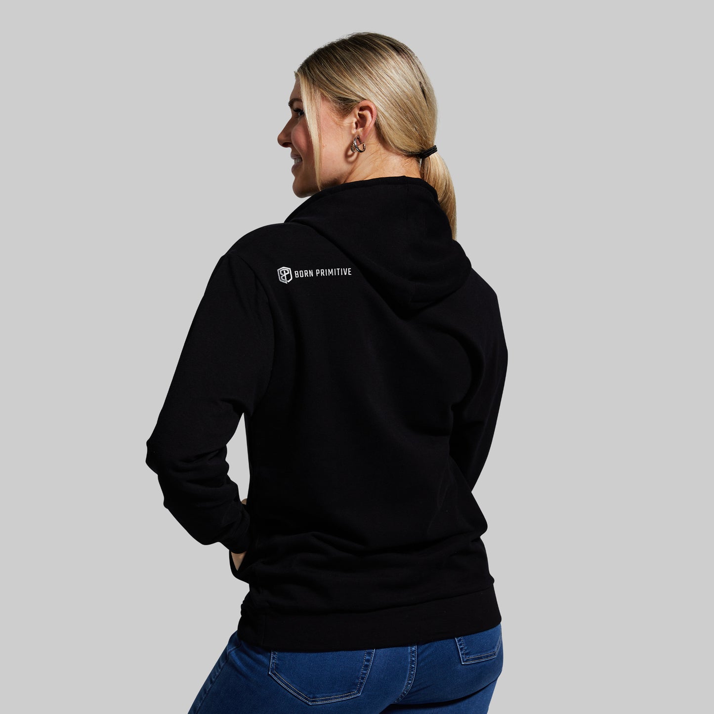 Person wearing a black hoodie with a logo on the back against a gray background