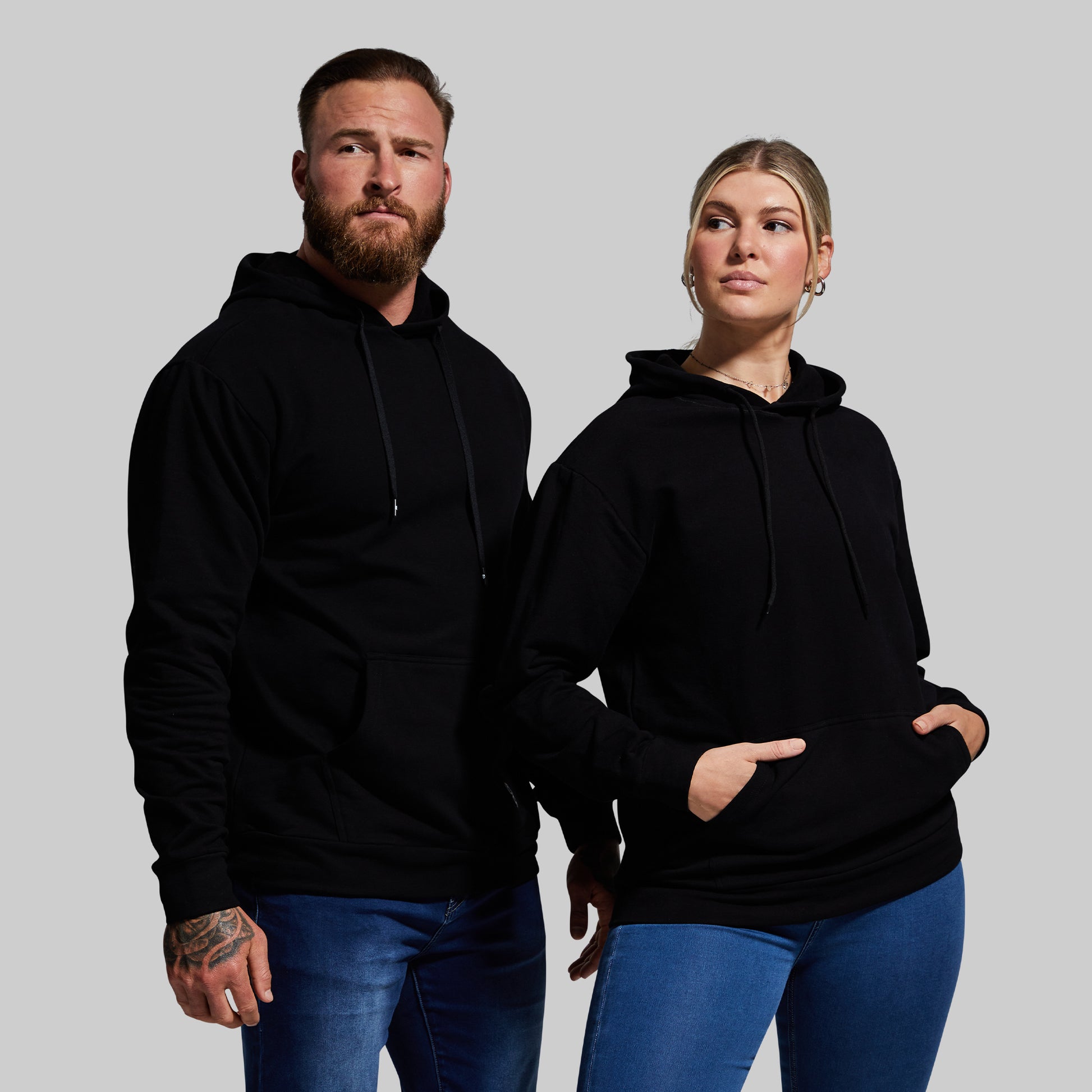 Two people wearing black hoodies and blue jeans against a gray background