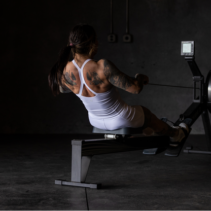 Person using a rowing machine in a dark indoor setting wearing a white sports bra.