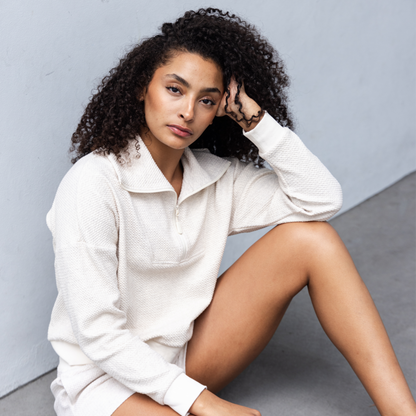 Woman in a white sweatshirt sitting on a gray surface with a neutral background