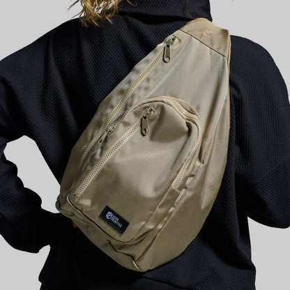 Beige sling bag worn over a dark jacket on a plain background
