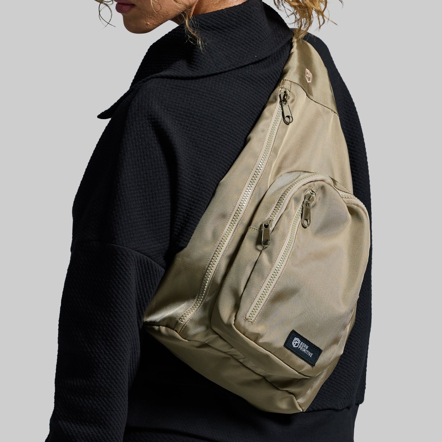 Beige sling bag worn by a person on a plain background