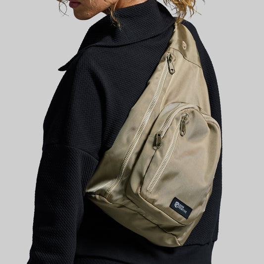 Beige sling bag worn by a person on a plain background