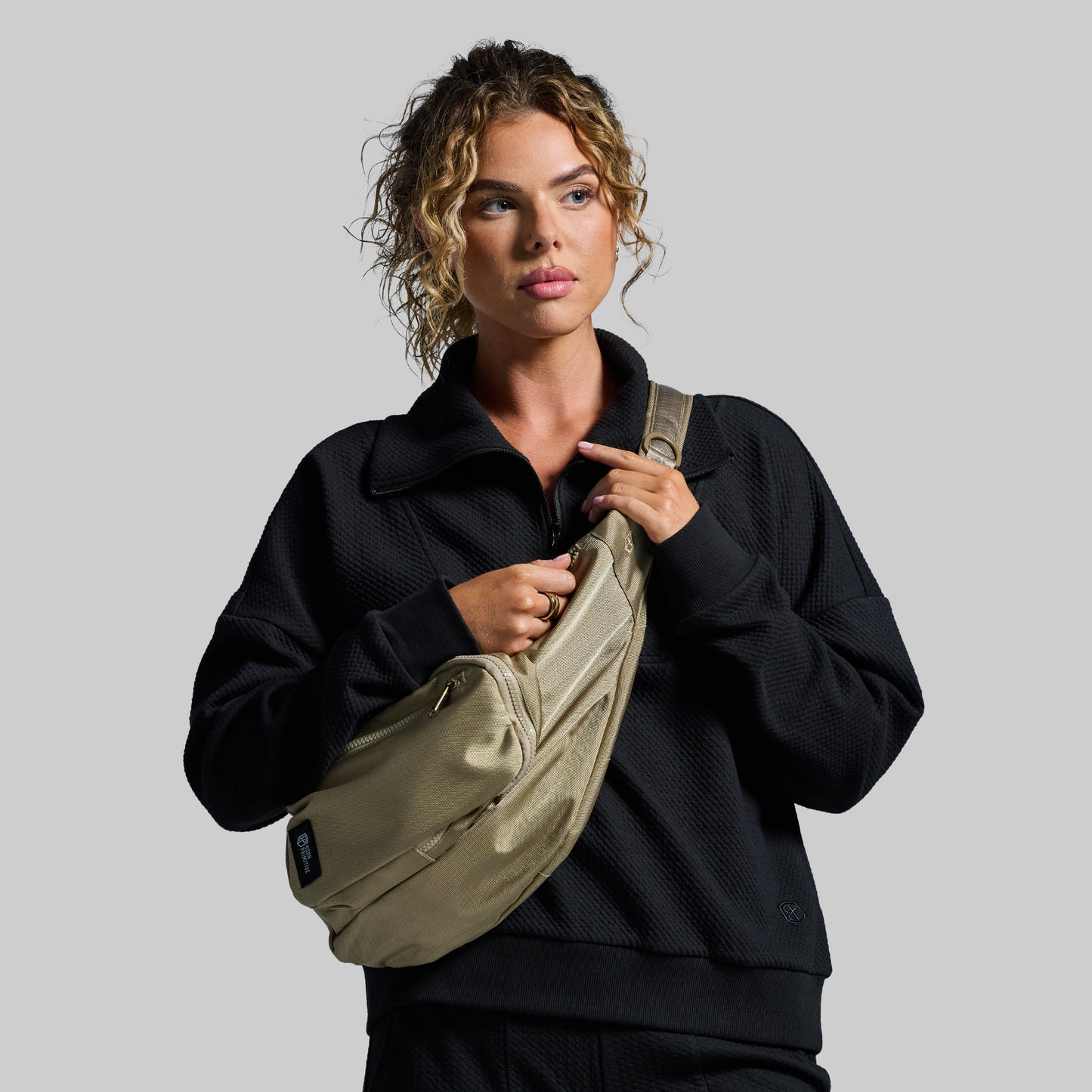 Woman holding a beige sling bag against a gray background