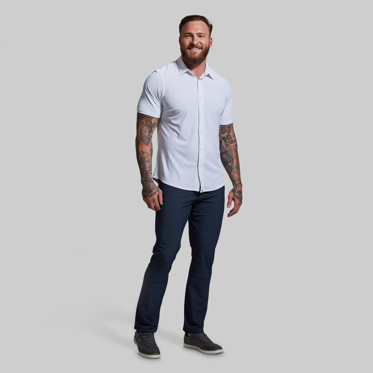 Man wearing a white short-sleeve shirt and navy blue pants on a gray background