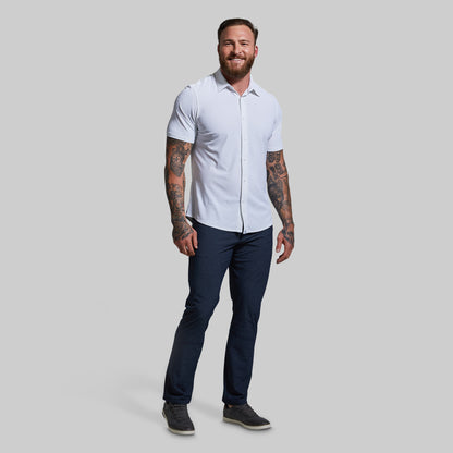 Man wearing a white short-sleeve shirt and navy blue pants on a gray background