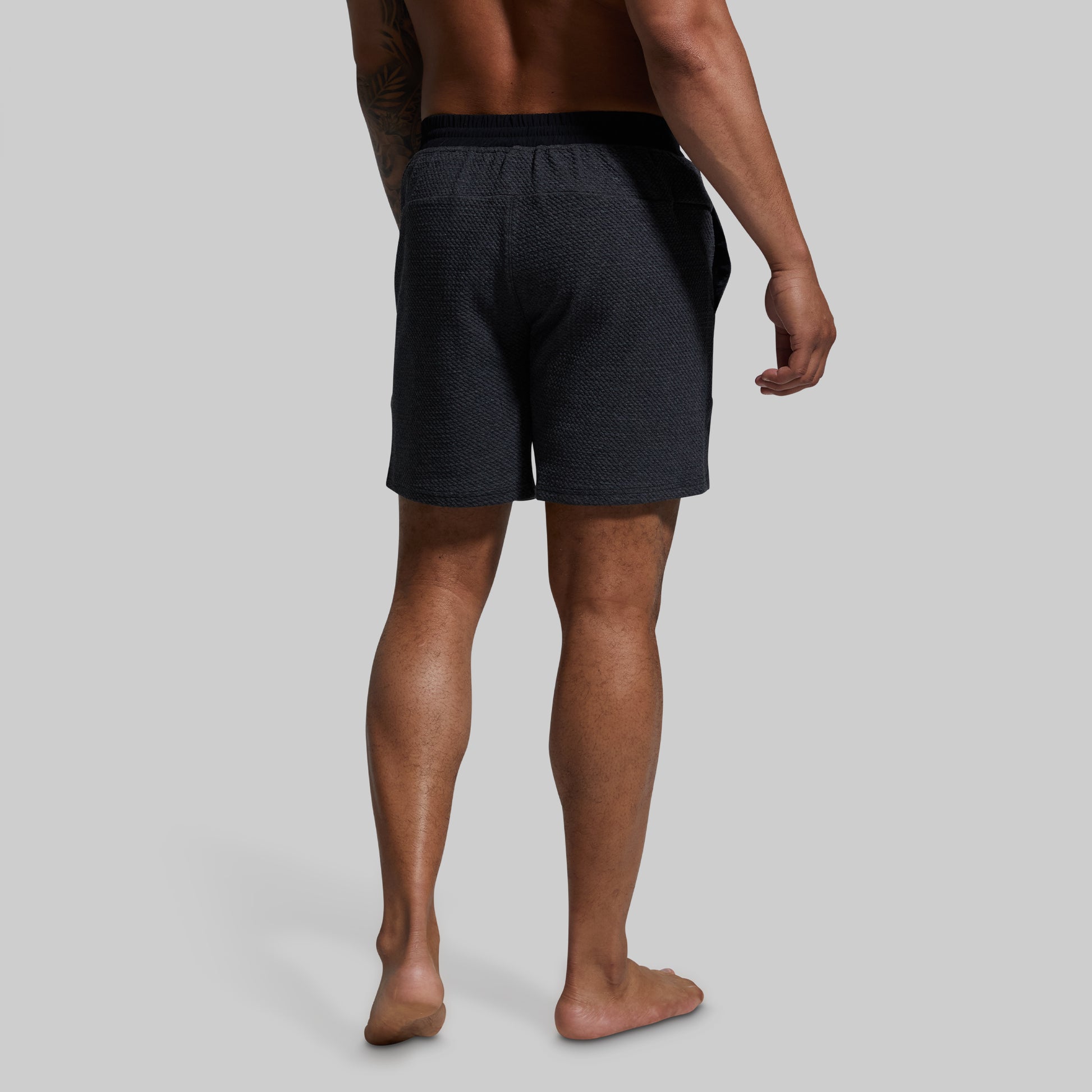 Person wearing dark gray shorts on a plain background