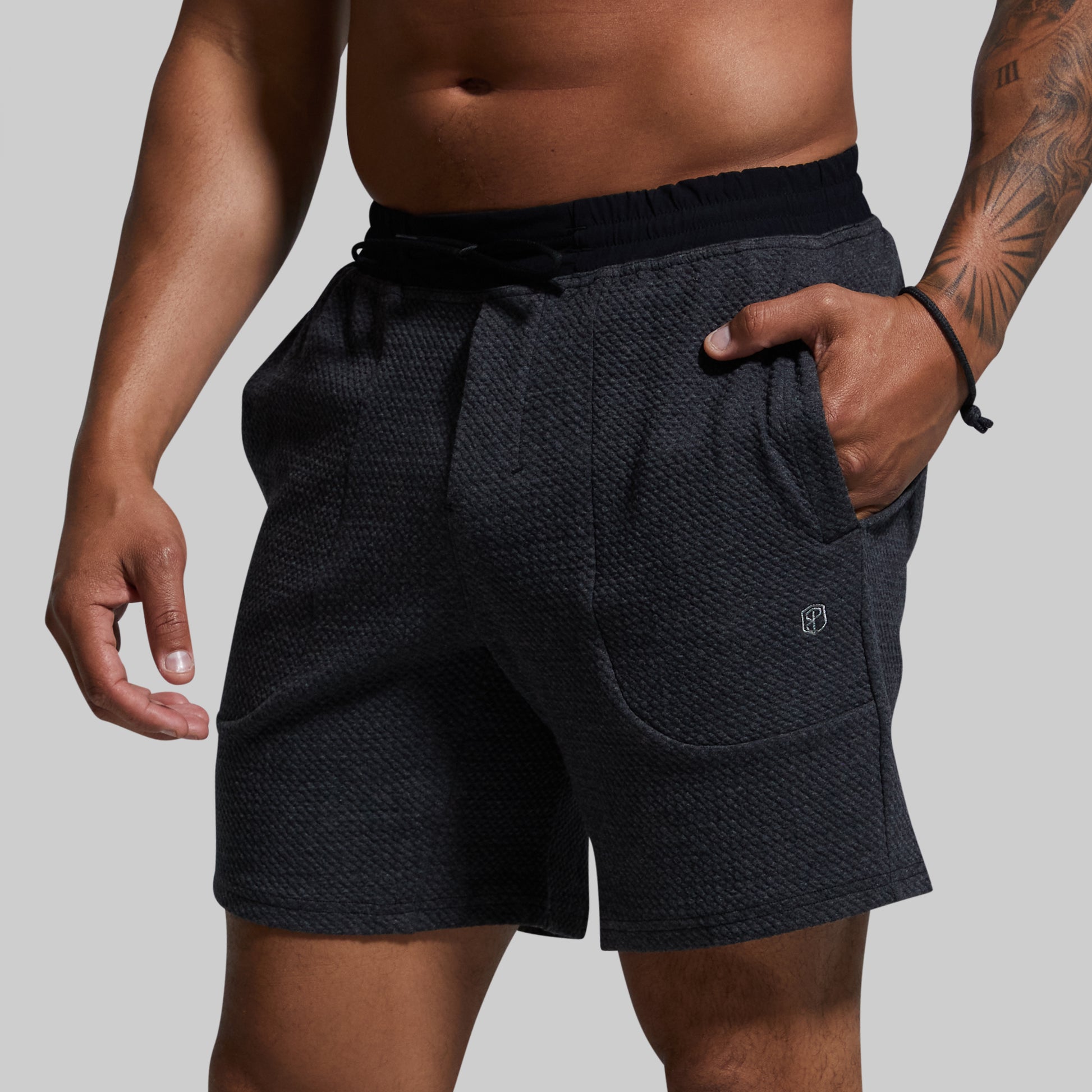 Person wearing dark gray textured shorts on a plain background