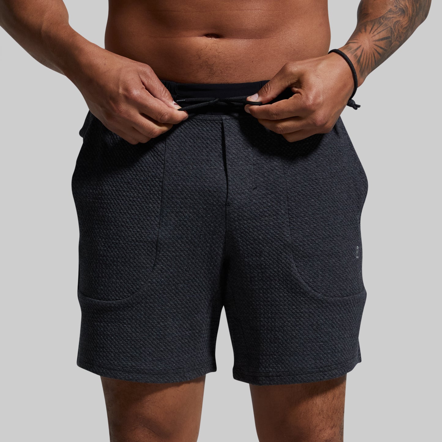 Person wearing dark gray shorts on a plain background