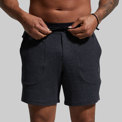 Person wearing dark gray shorts on a plain background