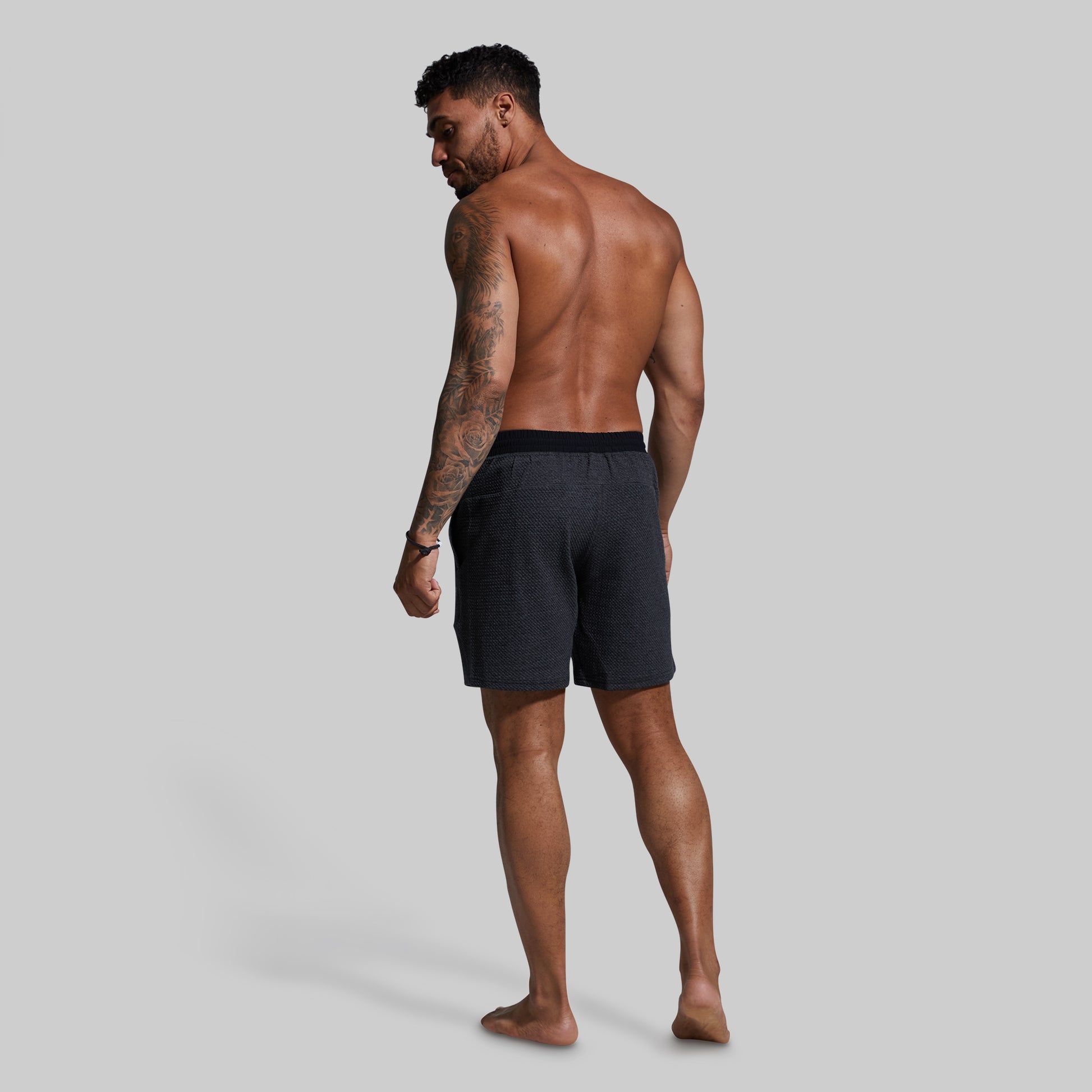 Man wearing dark gray shorts on a plain background