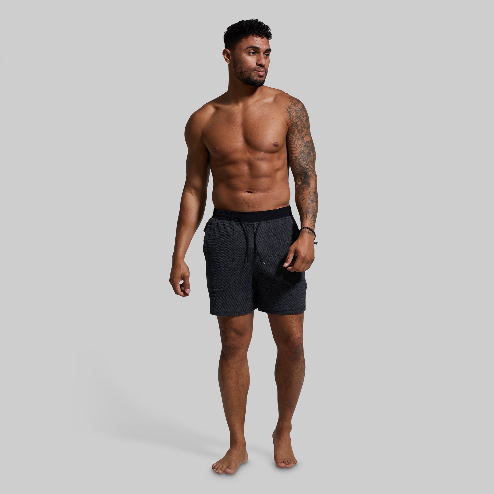 Man wearing dark gray lounge shorts on a gray background