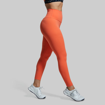 Person wearing bright orange leggings and white sneakers on a gray background