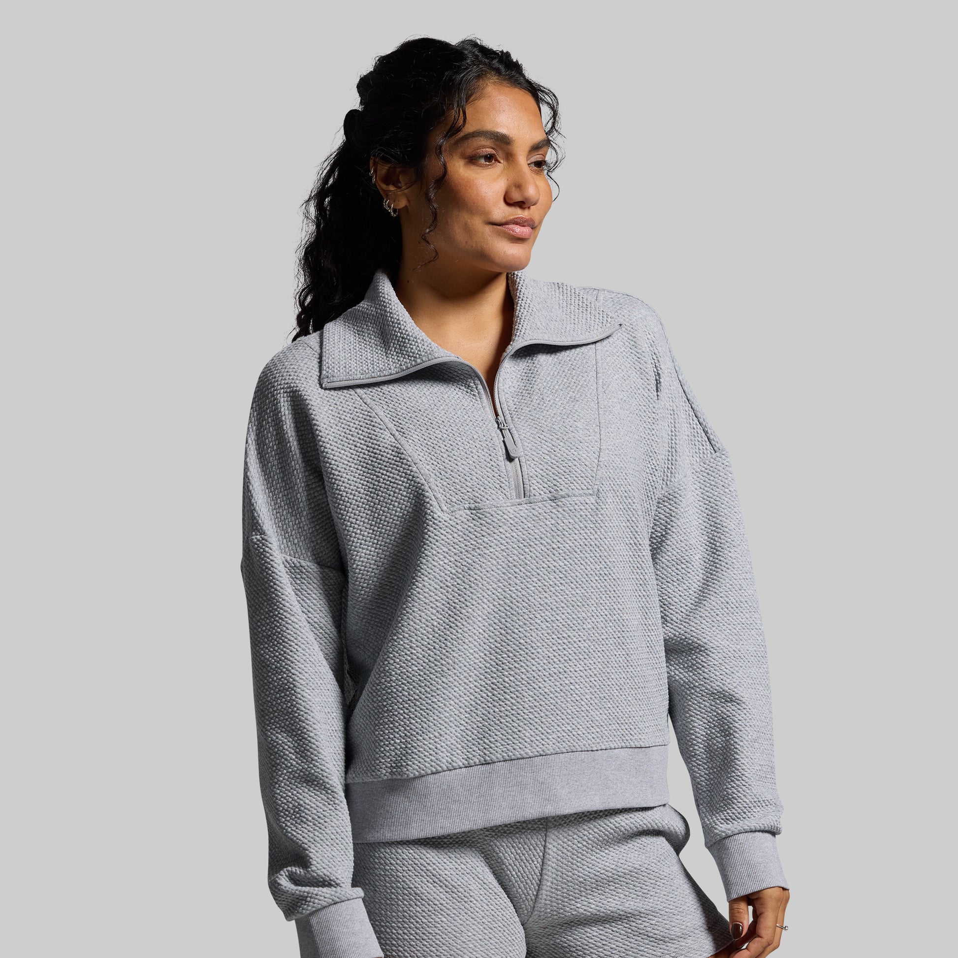 Woman wearing a gray textured pullover with a collar on a plain background