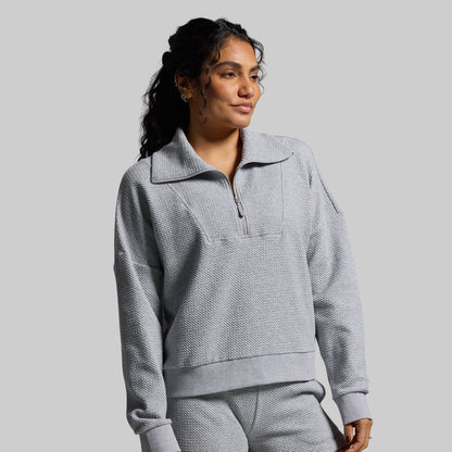 Woman wearing a gray textured pullover with a collar on a plain background