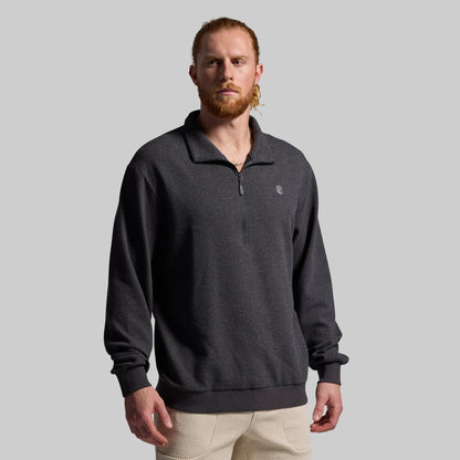 A man wearing a gray sweatshirt with a 1/4 zip front and a brand logo on the chest, paired with beige joggers.