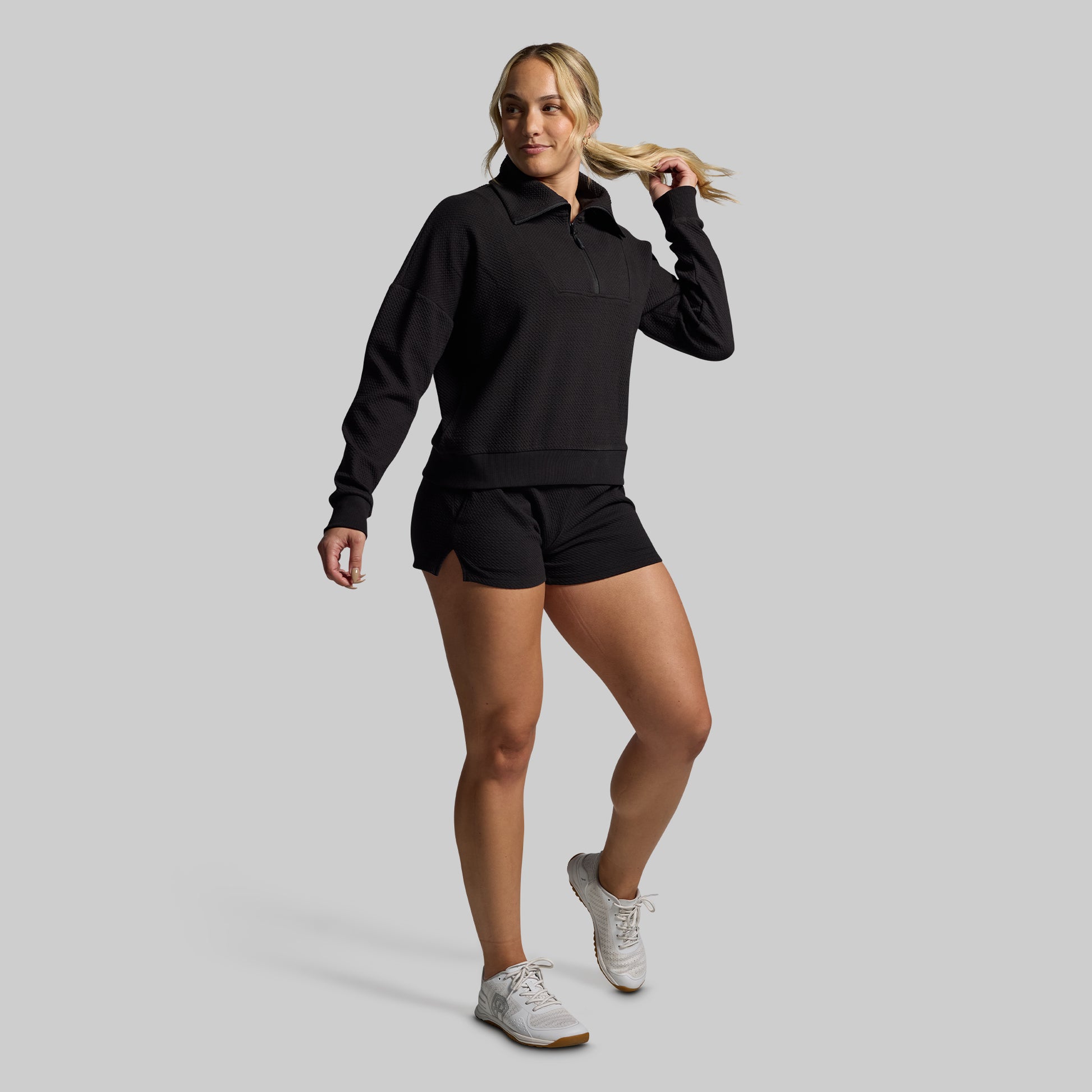 Woman wearing a black outfit with white sneakers on a gray background