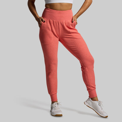 Person wearing coral pink jogger pants on a gray background