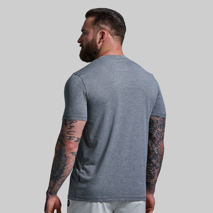 Man wearing a gray t-shirt with tattoos on arms against a plain background