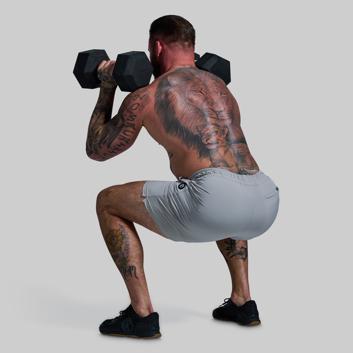 Man lifting weights with visible tattoos on a plain background