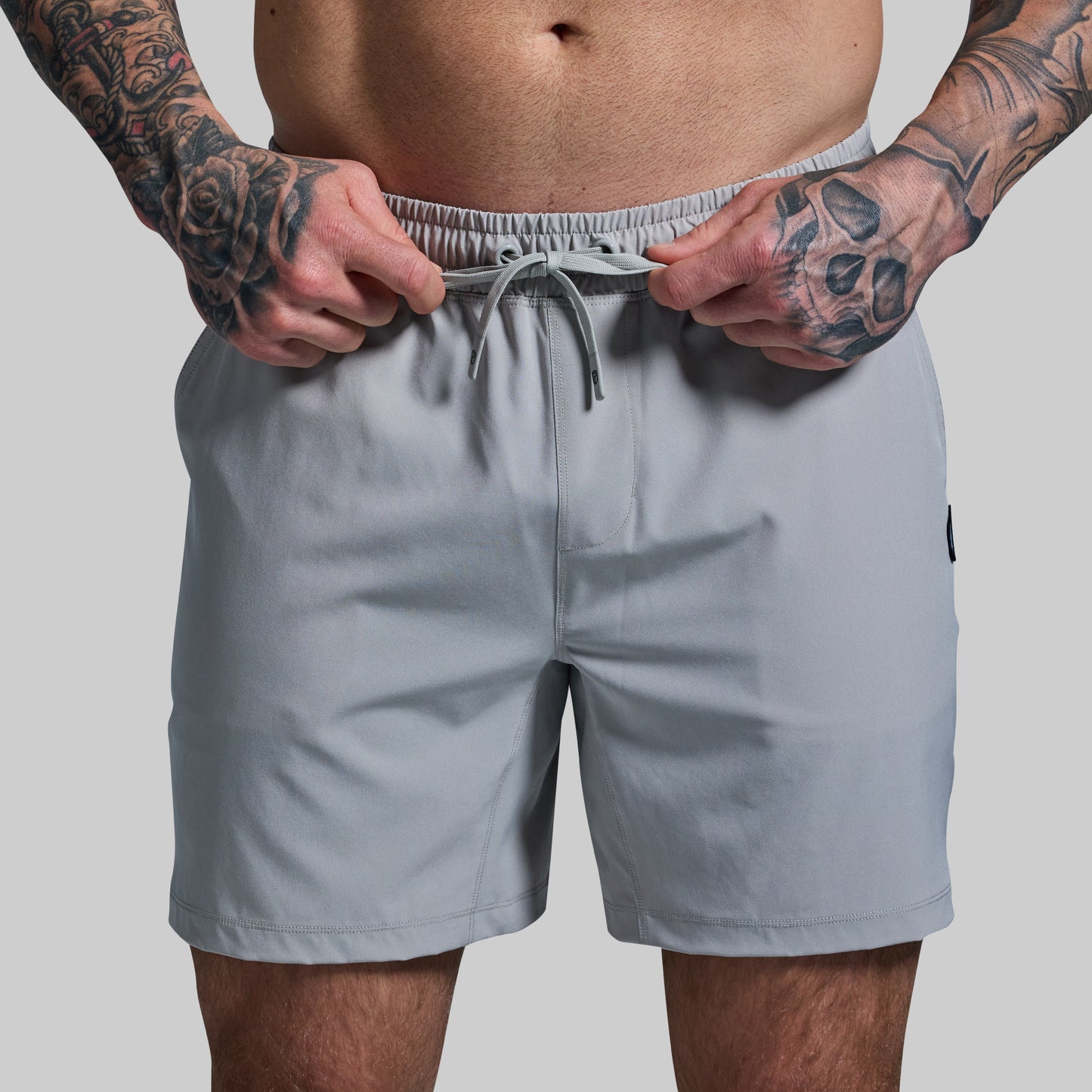Person wearing light gray shorts with a plain background