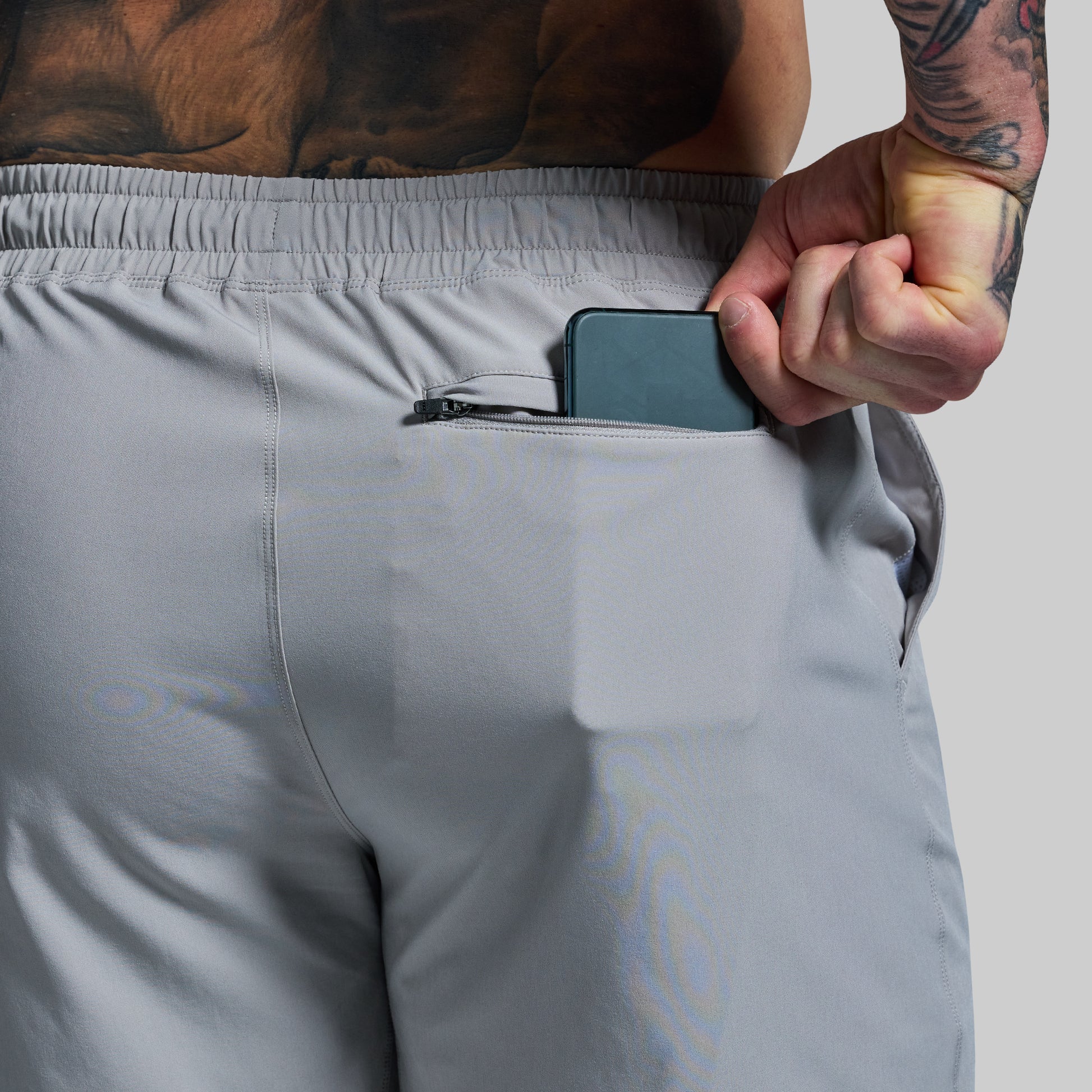 Person wearing gray shorts with a phone in the pocket against a neutral background