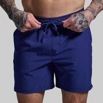 Person wearing blue shorts with tattooed arms on a gray background