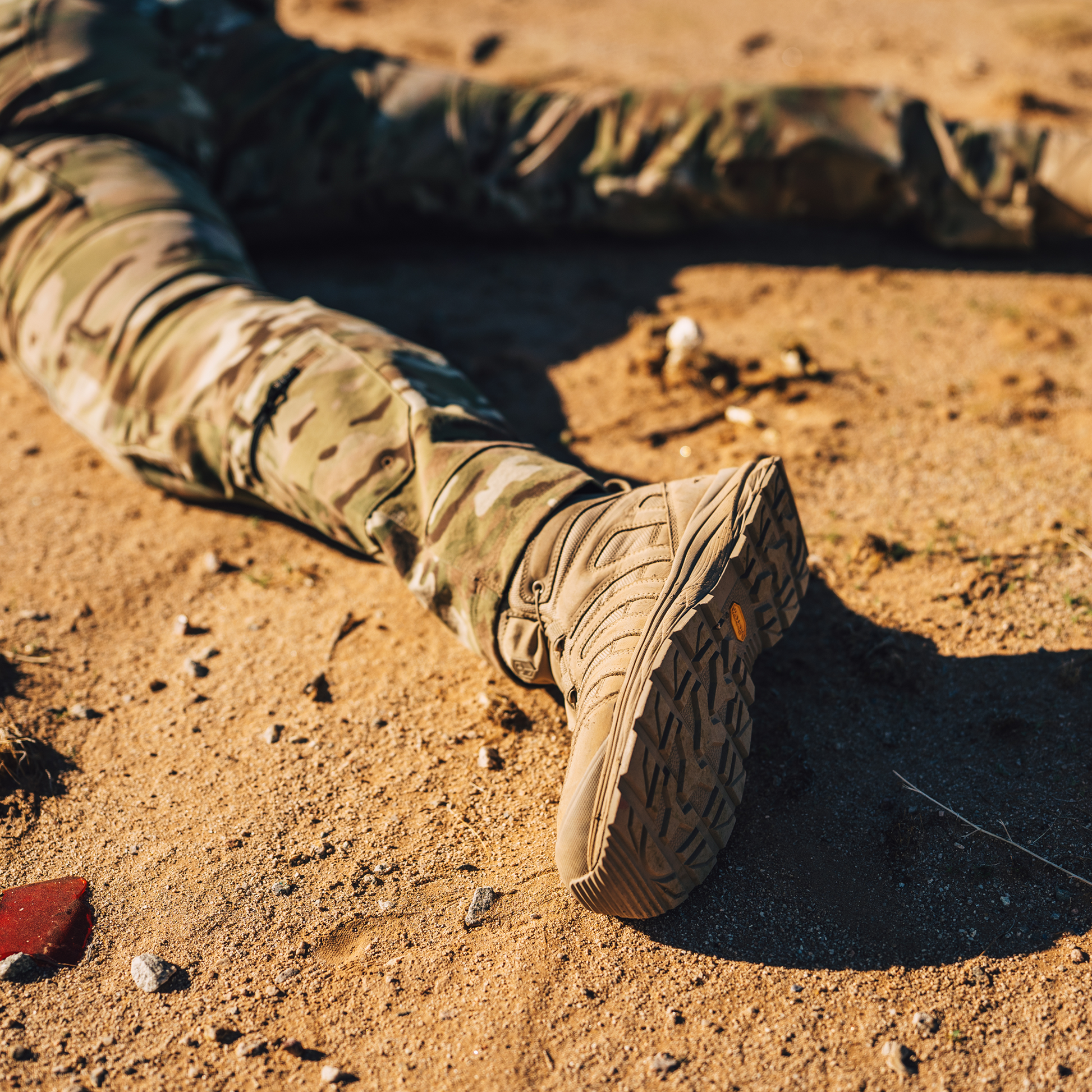 Person wearing camouflage pants and tan boots on a sandy ground