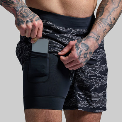 A person wearing black camouflage patterned versatile shorts with a compression liner and a phone held in the pocket.