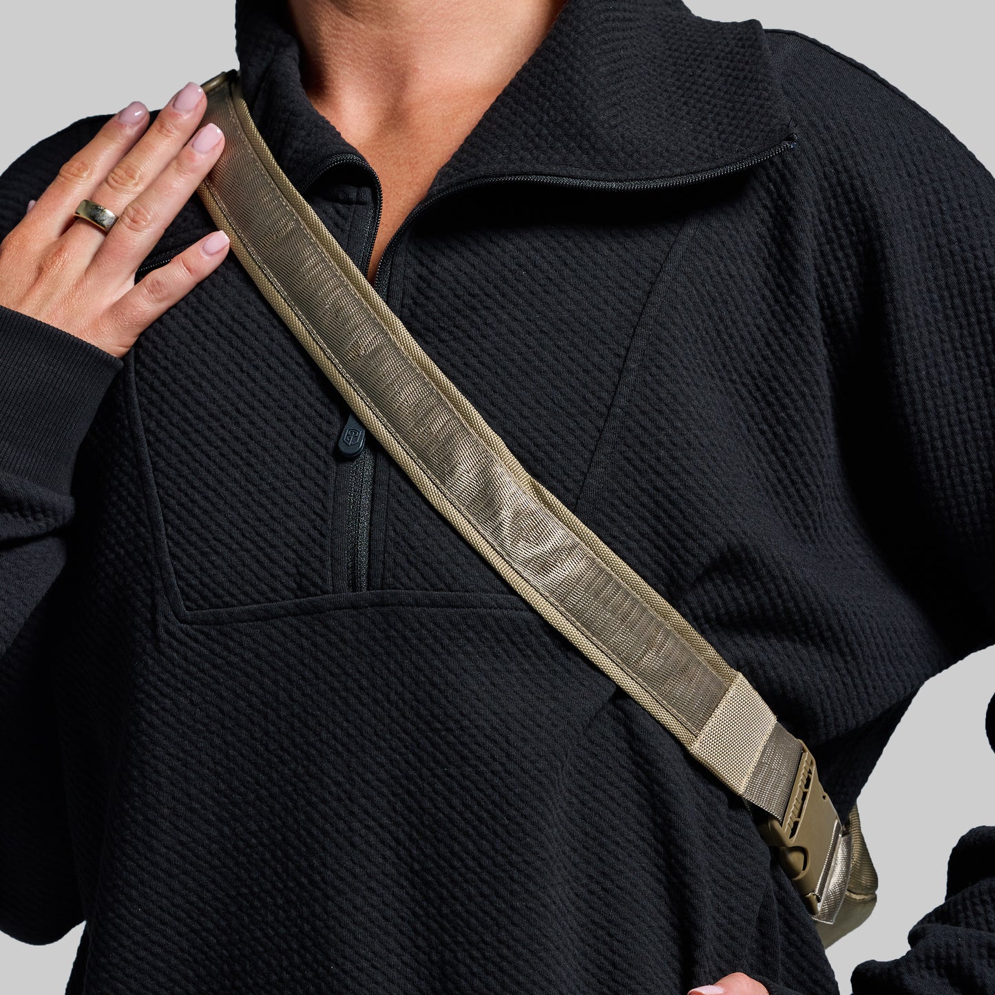 Person wearing a black jacket with a beige strap over their shoulder on a gray background