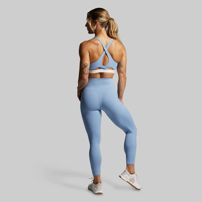 Woman wearing a blue sports bra and leggings on a gray background