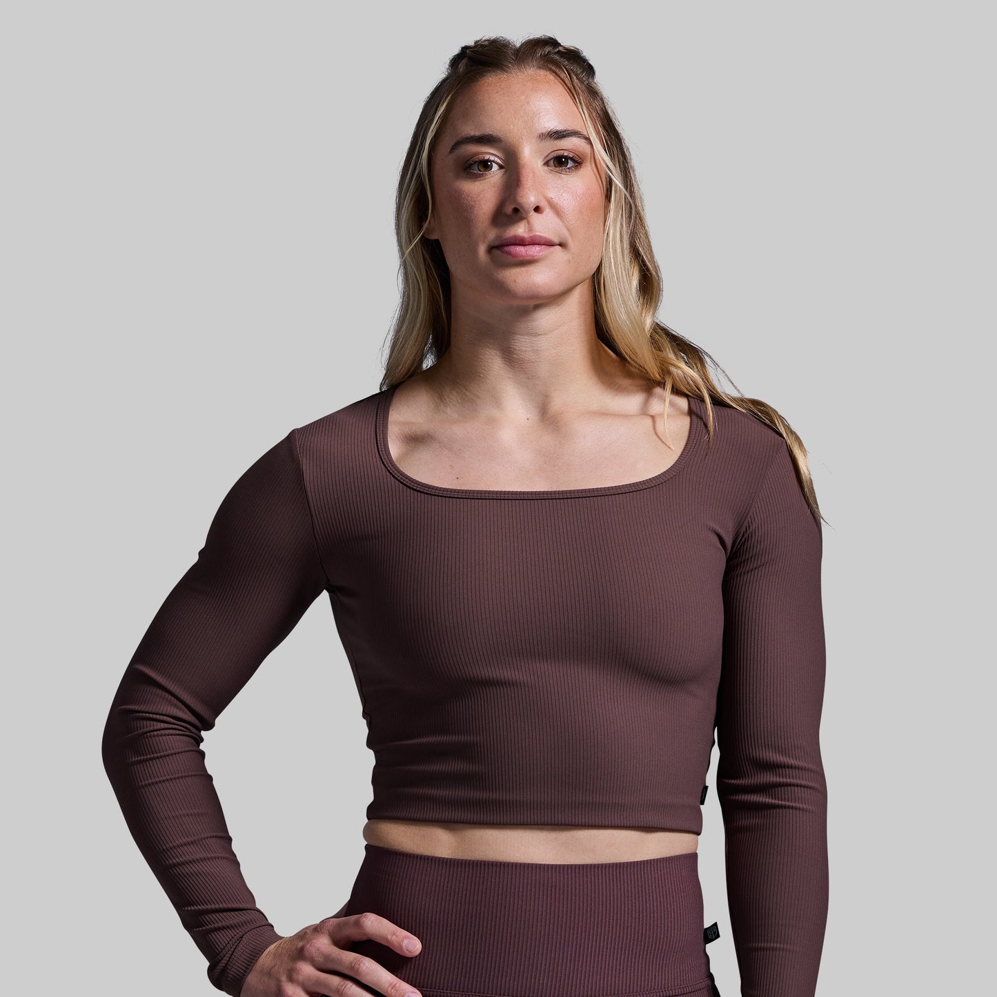 Woman wearing a brown long-sleeve crop top against a plain background