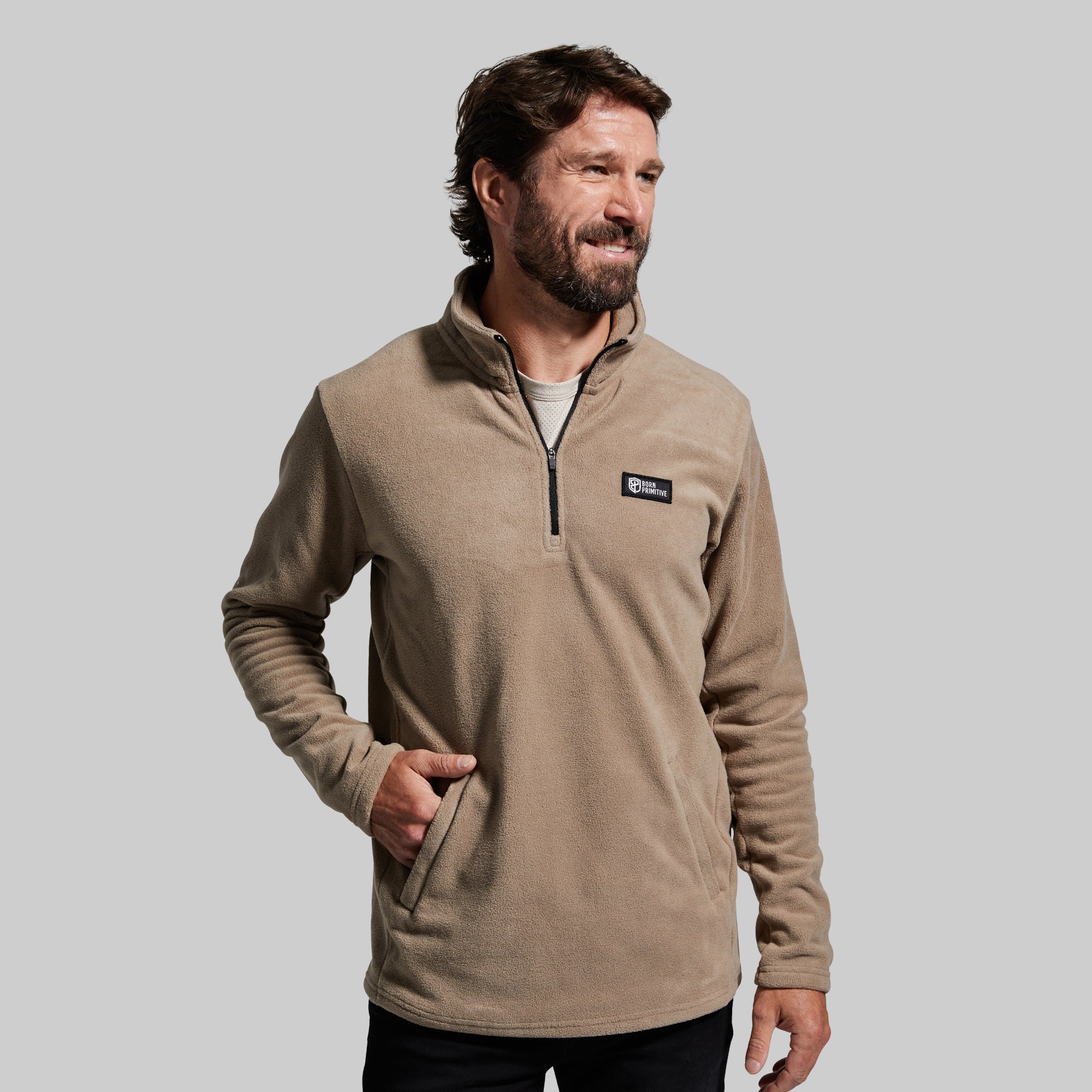 A man wearing a tan fleece quarter-zip pullover with two front zippered pockets.