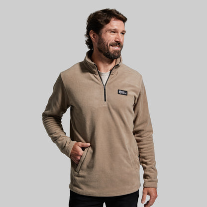 A man wearing a tan fleece quarter-zip pullover with two front zippered pockets.