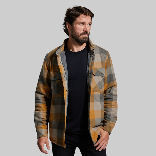 A man wearing a long sleeve, checkered, driftwood-colored jacket with collar, standing against a white background.