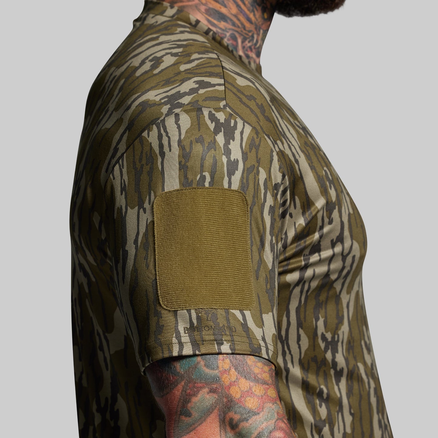Person wearing a camouflage shirt with a velcro patch on a gray background
