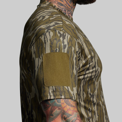 Person wearing a camouflage shirt with a velcro patch on a gray background