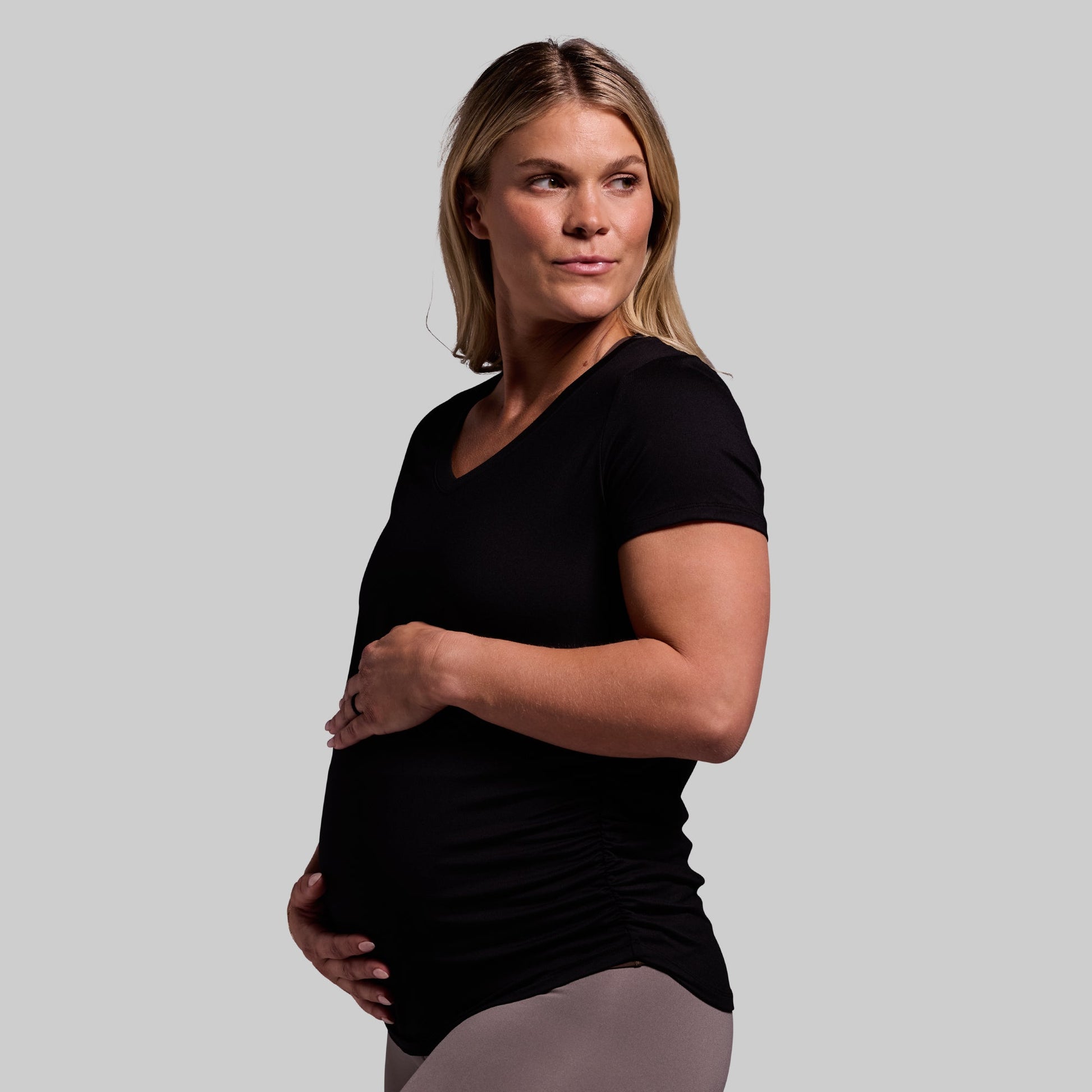 A pregnant woman wearing a black short sleeve V-neck top with enough room for her growing belly.